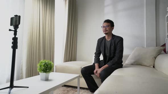 Asian man make a video call, interview, or conference sitting on a sofa with white concept room