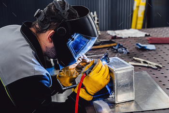 Man performs welding work at his workplace. Welding an aluminum tank with an argon welding machine.