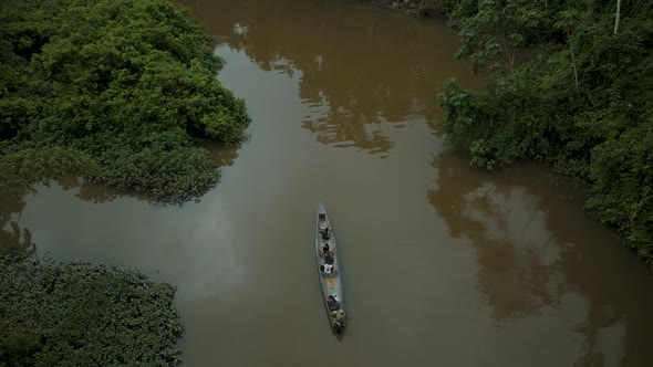 Aerial top down shot of tourist in boat cruising on amazon river surrounded by jungle plants in Peru