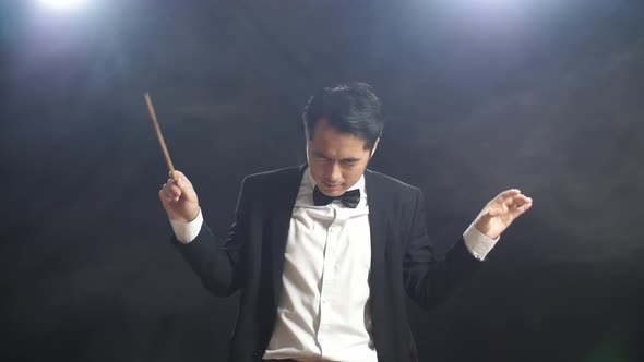 Asian Conductor Man Holding A Baton Closing His Eyes And Showing Gesture Quickly In The Black Studio