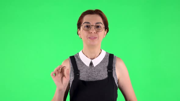 Portrait of Funny Girl in Round Glasses Is Waving Hand and Showing Gesture Come Here. Green Screen