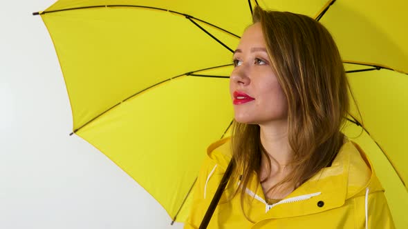 A girl in a yellow raincoat under an umbrella looks up. Isolated on white background