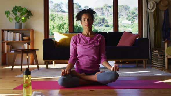 Mixed race woman practicing yoga and meditating while sitting on yoga mat at home