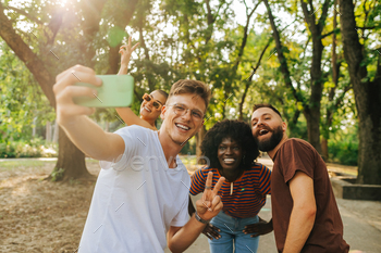 A multicultural group of friends are posing to take a selfie outside.