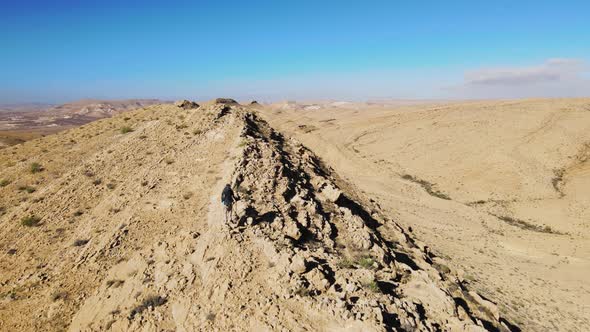 Aerial Flying Over Male Hiker Walking Along Ridge Line In The Negev Desert Located In Israel. Dolly