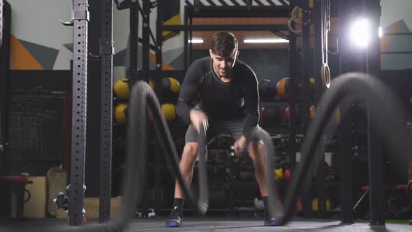 Athletic Young Caucasian Man Doing Exercises with Rope at Gym