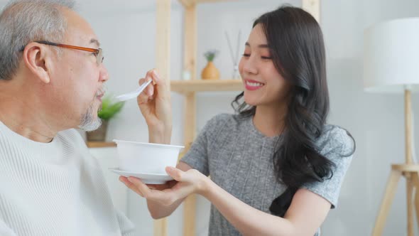 Asian attractive young daughter serving food to senior father in house.