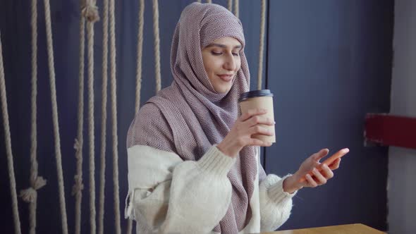 Muslim Girl in a Cafe with a Smartphone