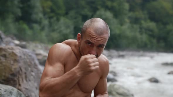 an Unshaven Man with a Bare Torso Trains By a Mountain River