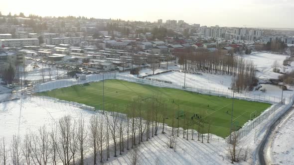 Shot over a Vibrant Green Football Field in Iceland, Soccer Pitch surrounded by Snow