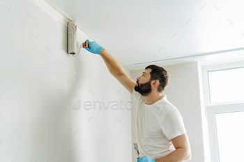 caucasian bearded man painting wall with paint roller. Painting apartment, renovating home