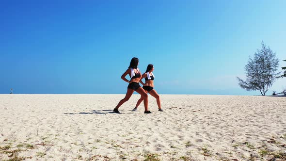 Young happy ladies on photoshoot in the sun at the beach on clean white sand and blue background 4K