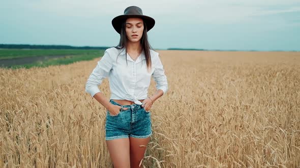 Beautiful Girl in a Shorts and Hat Walking Through a Wheat Field at Sunset. Freedom Concept. Wheat