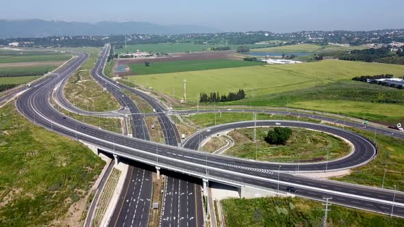 aerial slow forward drone shot of a highway interchange, surrounded by fields, green grass end trees