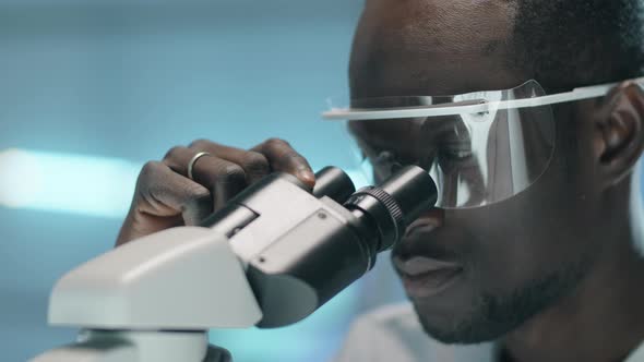 Afro-American Scientist Looking through Microscope in Lab