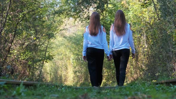 Twins Girls Holding Hands Walking Along Railroad Tracks