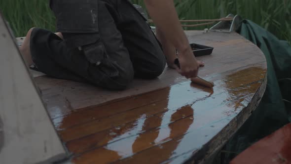 Carpenter sealing bow of wooden boat deck with ultra violet protection varnish using roller.