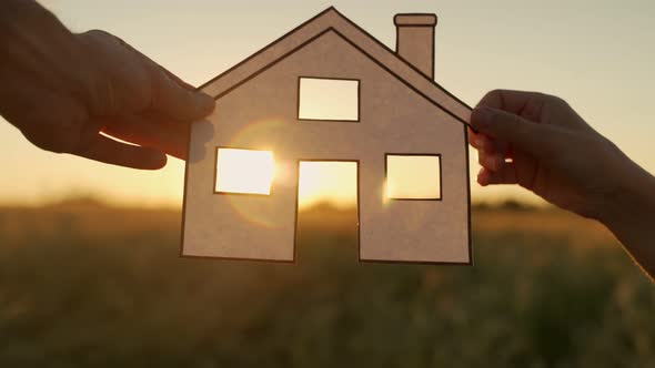 Family Holds Paper House at Sunset Sun Shines Through Window