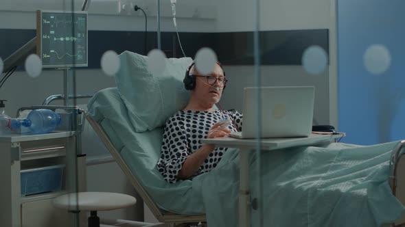 Elder Patient Using Laptop and Headphones in Hospital Ward