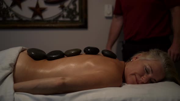 Medium shot of a mature caucasian topless woman with stones in a row down her back.  Woman has smile