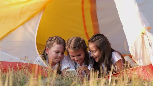 Beautiful girls gossip lying together in a tent while camping in the summer forest during summer