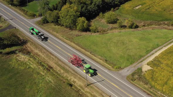 farm tractors driving down the road in the country while towing equipment
