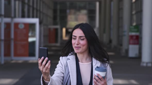 Businesswoman with travel mug having video call on her smartphone