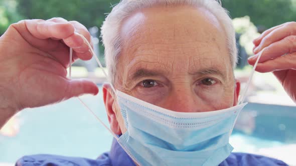 Portrait of senior caucasian man with grey hair putting face mask on looking at camera in slow motio