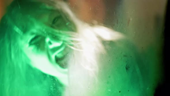 Scary ghost woman screaming through dirty glass on dark background.