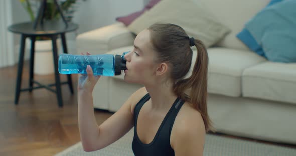 Young and Fit Woman Sitting on the Floor at Home After Intensive Sport Workout and Drinking Water