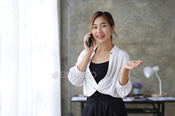 Beautiful Asian businesswoman or manager in the office standing on the phone with a partnership.