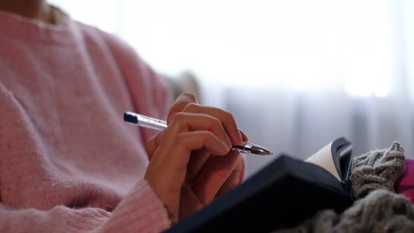 Unrecognizable Woman in Warm Knitted Sweater Writes Down Plans or Tasks for the New Year