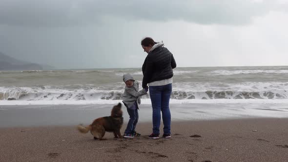 Young Woman Holds Her Child By Hand While Walking Along the Beach in Cloudy Weather in the Offseason