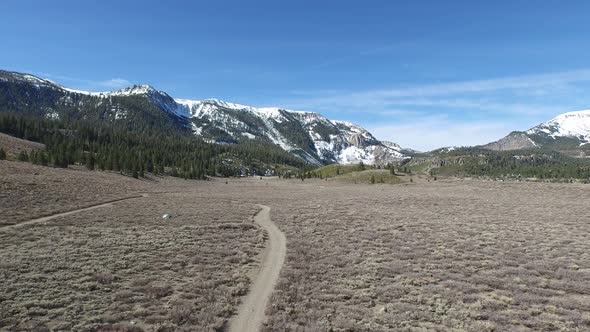 Aerial shot of hiking trail in a meadow below a scenic mountain