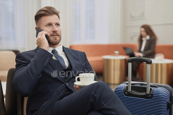 Businessman with Suitcase Speaking on Phone in Hotel