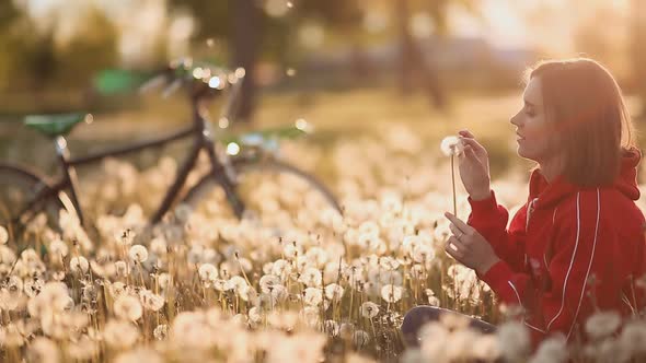 Female Sitting and Blowing a Dandelion