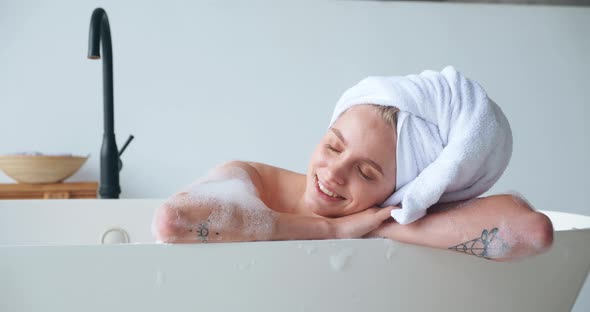 Attractive Blonde Woman with Closed Eyes of Pleasure Wrapping Her Head in a Bath Towel Lying in