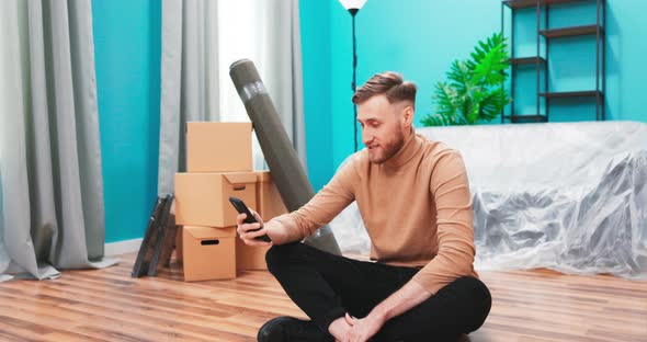 Puzzled Man Look at Smartphone Device Relocate in New Apartment Search Furniture for Their Flat