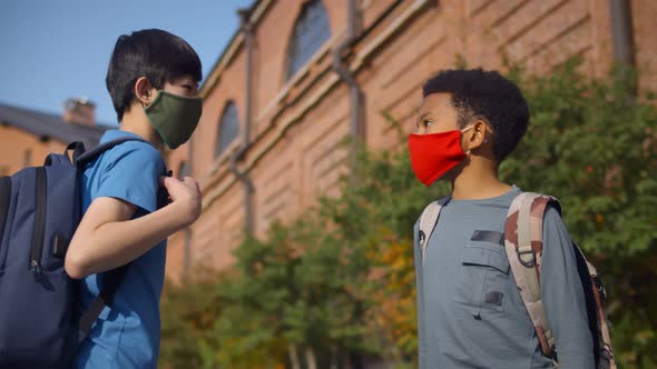 Side View of Diverse Schoolboys in Protective Mask Doing Elbow Greeting Outdoors