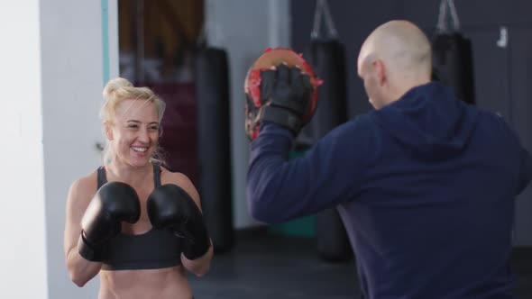 Caucasian female boxer wearing boxing gloves training her punches with male trainer at the gym