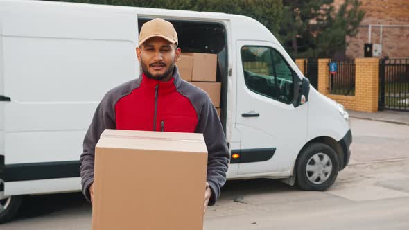 Delivery Boy Holding A Cardboard Box Moving The Box Towards The Camera Smiling