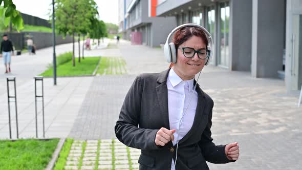 Portrait of a Smiling Woman in a Business Suit Listening to Music in Headphones Outdoors