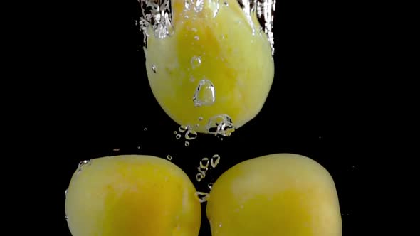 Super slow motion, fresh apricots fall into the water with air bubbles