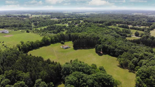 A high forward aerial view of the Ohio landscape. Small farmhouse below. Camera tilts up to summer c