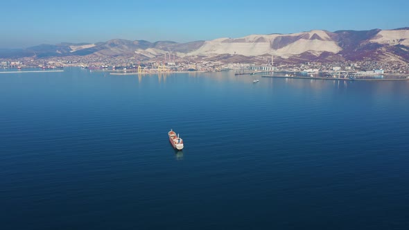 Aerial View Following the Ultra Large Cargo Ship at Sea Leaves Port at Sunny Day