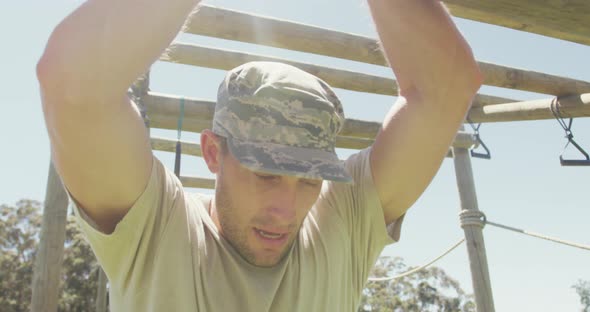 Tired caucasian male soldier hanging on monkey bars on army style obstacle course in the sun alt