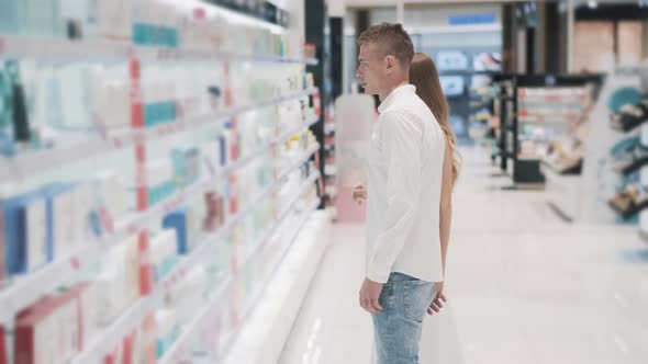 Pretty Woman and a Slender Guy Are Choosing Cosmetics at Shop