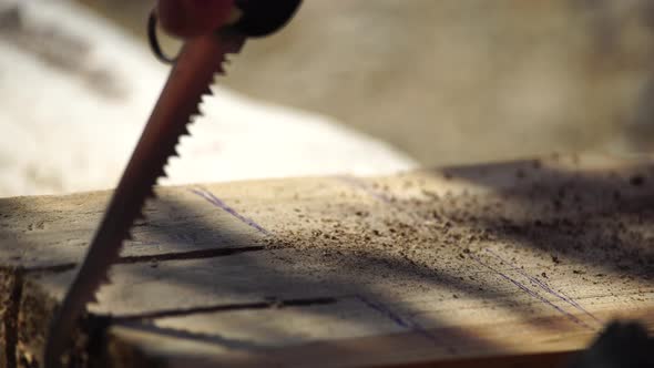 Man Hands Using a Swiss Knife Sawing a Piece of Wood Plank Outdoor Survival and Camping Fun in the