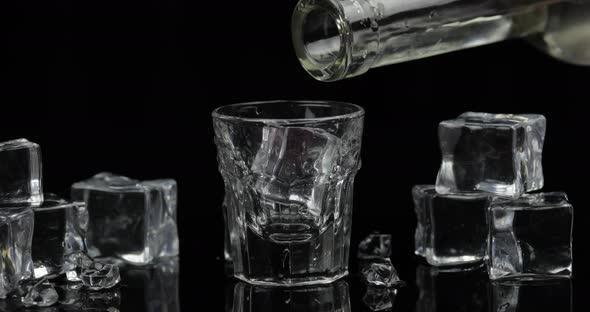 Pouring Up Shot of Vodka From a Bottle Into Glass. Black Background