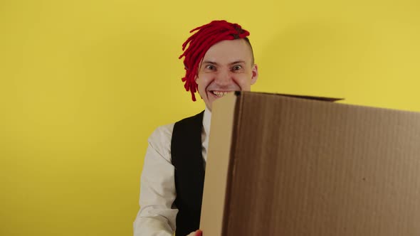 Young Crazy Man with Cardboard Box on Yellow Background in Studio